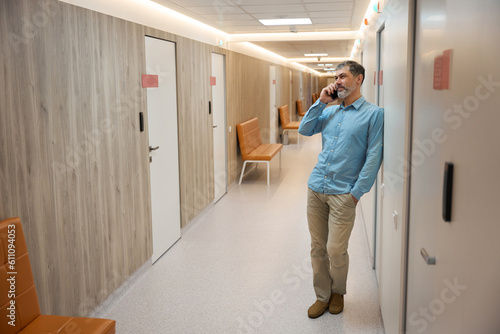 Adult man leaning against wall talking on phone in clinic