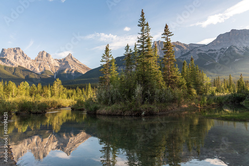Views near Banff National Park in summer time with stunning reflection in calm water below iconic mountain peaks at Three Sisters. Tourism, travel, popular area. 