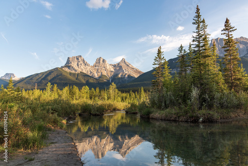 Views near Banff National Park in summer time with stunning reflection in calm water below iconic mountain peaks at Three Sisters. Tourism, travel, popular area. 