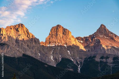 Three Sisters in Canmore seen at golden hour, sunset with mountain peaks shining bright with sunshine. Beautiful, pristine, famous, tourist area, Banff National Park. 