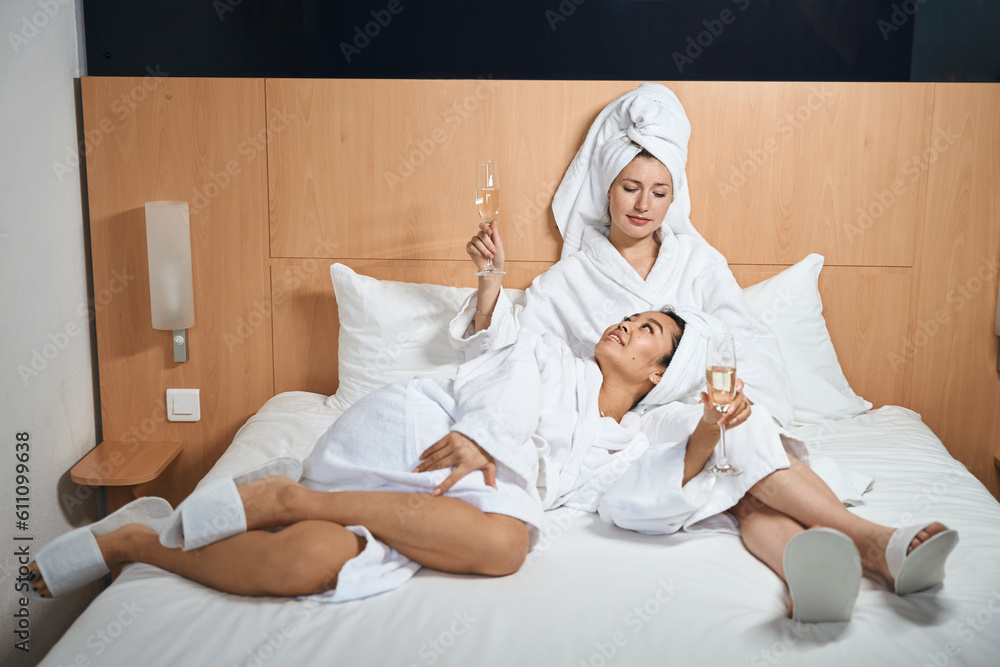Two happy girlfriends drinking champagne in white bathrobes in hotel Two happy girlfriends drinking champagne in white bathrobes in hotel