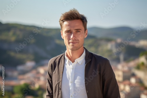 Headshot portrait photography of a glad boy in his 30s wearing an elegant long-sleeve shirt against a scenic cliffside village background. With generative AI technology