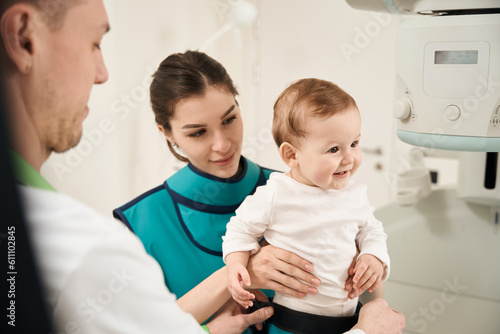 Experienced radiographer preparing little patient for diagnostic radiography photo