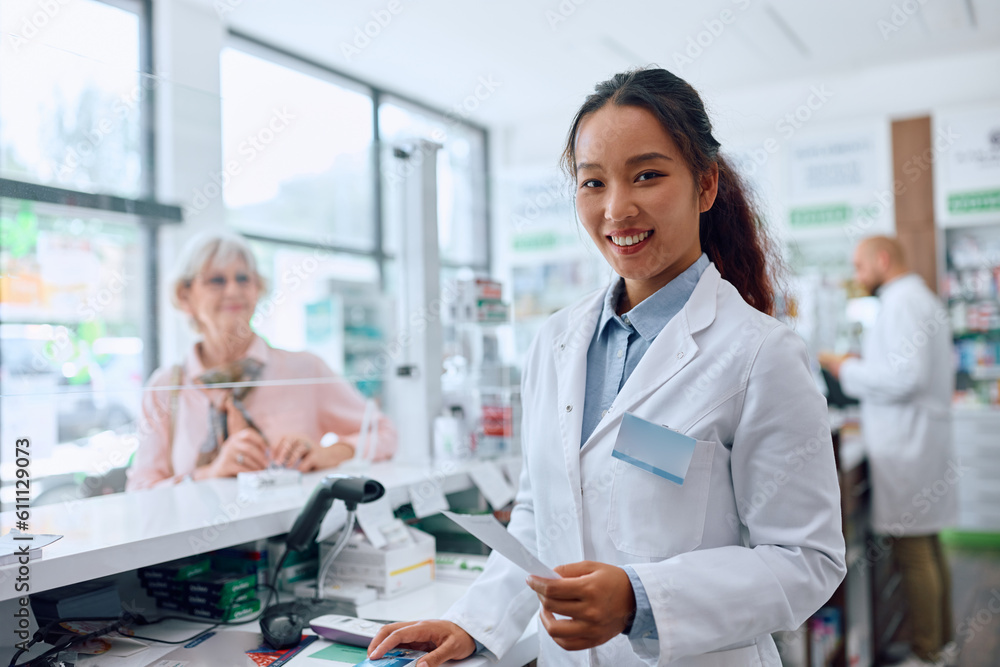 Obraz premium Happy Chinese female pharmacist working in pharmacy and looking at camera.