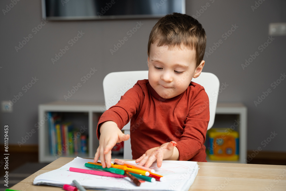 A cute little toddler boy of two years old draws with markers in the album in the children's room at home. Educational activities for kids. Selective focus A cute little toddler boy of two years old draws with markers in the album in the children's room at home. Educational activities for kids. Selective focus