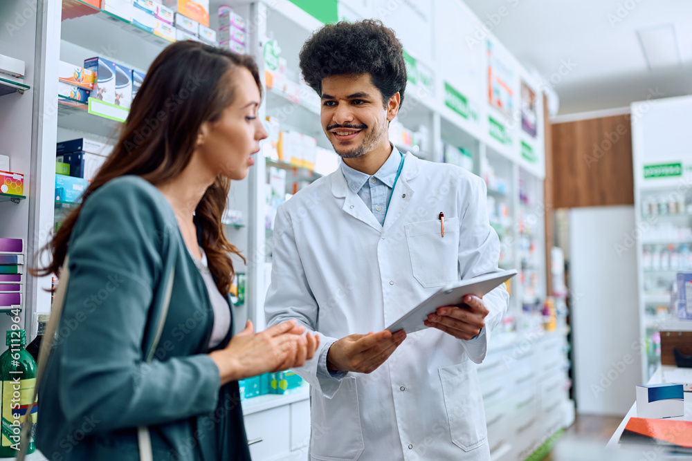 Obraz premium Happy pharmacist and his female customer using touchpad in pharmacy.