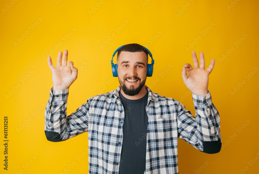 Happy caucasian guy shows a good gesture, agrees with something, claims that everything is fine, smiles broadly, wears headphones, enjoys isolated on a yellow background Happy caucasian guy shows a good gesture, agrees with something, claims that everything is fine, smiles broadly, wears headphones, enjoys isolated on a yellow background