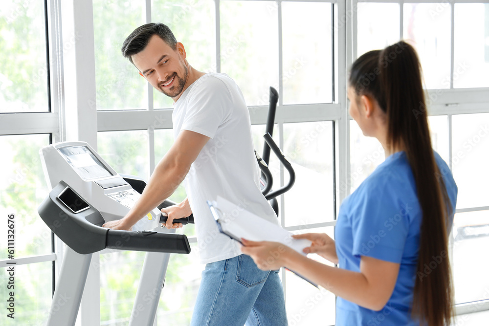 Fototapeta premium Female physiotherapist working with young man on treadmill in rehabilitation center