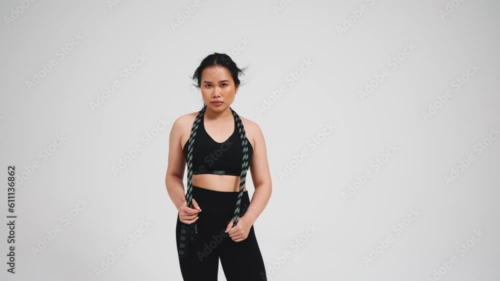 Pretty asian woman holding skipping rope in black tracksuit against gray background in studio Pretty asian woman holding skipping rope in black tracksuit against gray background in studio