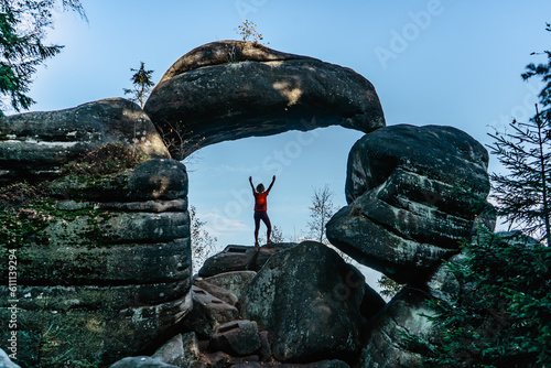 Woman hiker in Rock Gate in nature reserve of Broumov Walls, Czech Republic.Old sandstone rock formation in Broumovske steny.Active female traveler standing on rock enjoying views,success,adventure