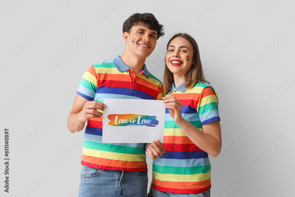 Young couple holding paper with text LOVE IS LOVE on light background. Pride Month Young couple holding paper with text LOVE IS LOVE on light background. Pride Month