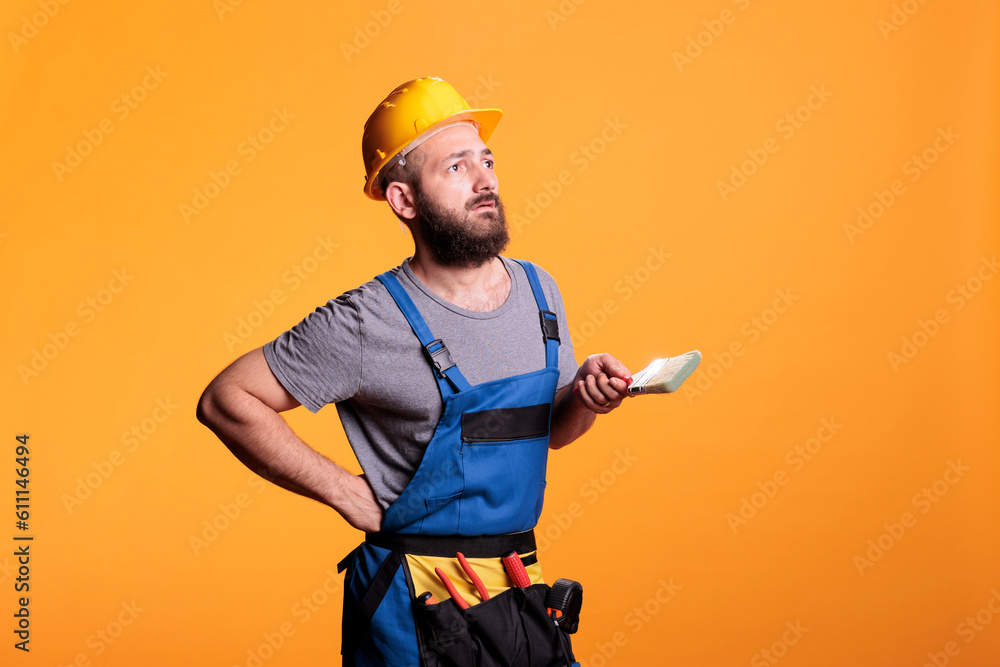 Confident handyman holding paintbrush to color walls, working on refurbishment project and painting with tools. Construction worker painter doing renovation work with brush and paint.
