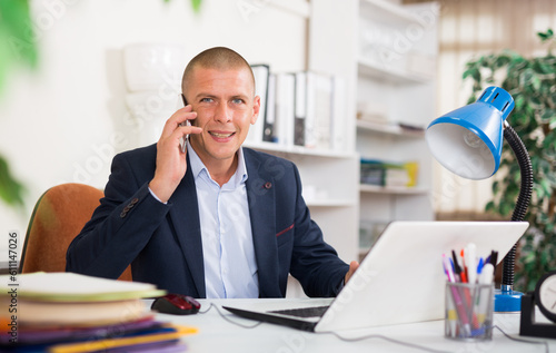 Portrait of focused manager sitting at office table, having phone conversation