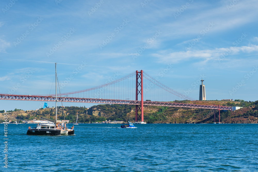 View of 25 de Abril Bridge famous tourist landmark over Tagus river, Christ the King monument and a tourist yacht boat. Lisbon, Portugal