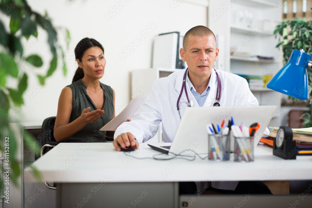 Middle aged asian female patient visits young doctor in office at the hospital