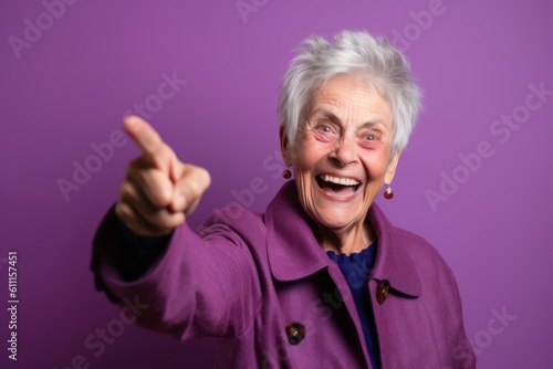 Close-up portrait photography of a grinning mature woman raising a finger as if having an idea against a vibrant purple background. With generative AI technology