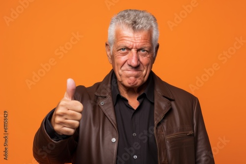 Close-up portrait photography of a satisfied mature man showing a thumb down against a bright orange background. With generative AI technology