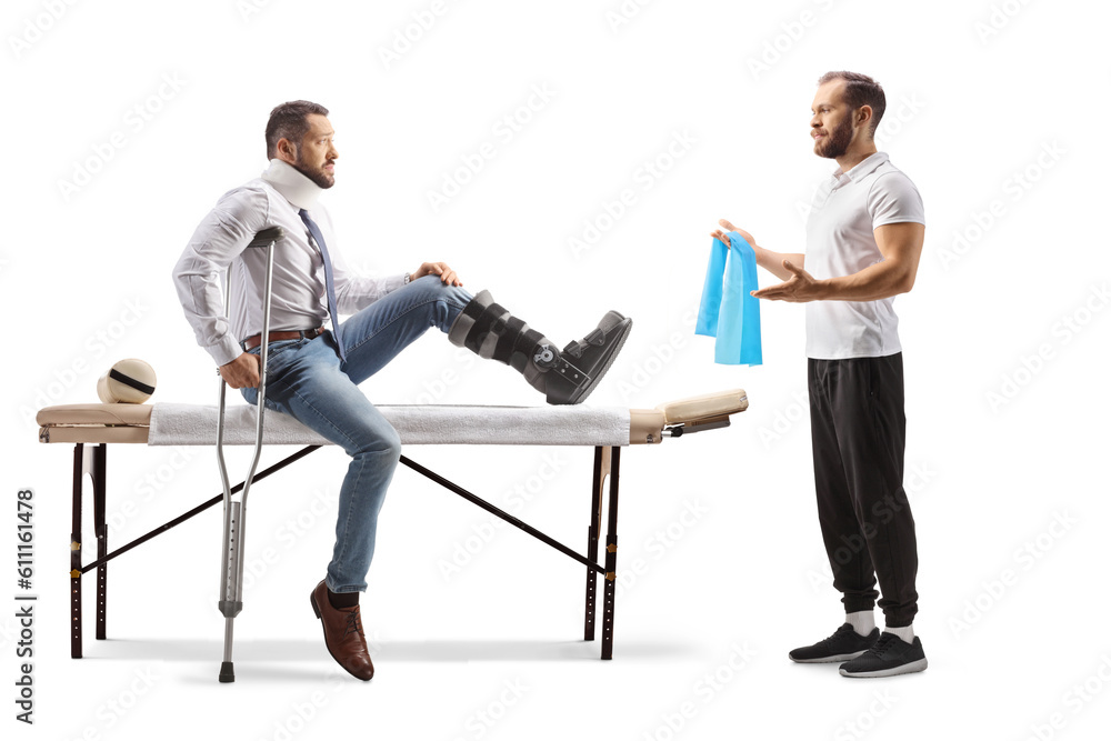 Obraz premium Young male patient sitting on a therapy bed with a brace on his leg and a therapist showing exercises with a resistance band