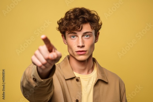 Headshot portrait photography of a glad boy in his 20s raising a finger as if having an idea against a pastel yellow background. With generative AI technology