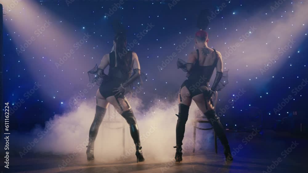 Sensual women posing on chairs in lace lingerie costumes. Gorgeous show girls dancing hidden by mysterious smoke on dark stage with two spotlights. Seductive model girls looking camera with passion 4K Sensual women posing on chairs in lace lingerie costumes. Gorgeous show girls dancing hidden by mysterious smoke on dark stage with two spotlights. Seductive model girls looking camera with passion 4K