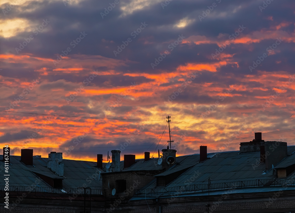 Sunset clouds over the roof of a large house with antennas and wires