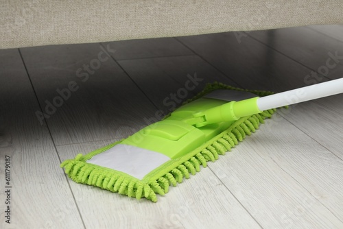 Cleaning white parquet floor under sofa with mop  closeup