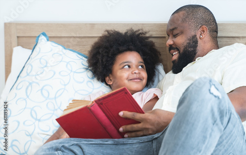 Obraz na płótnie African family, single father and cute boy, lying on bed, reading a book together at home