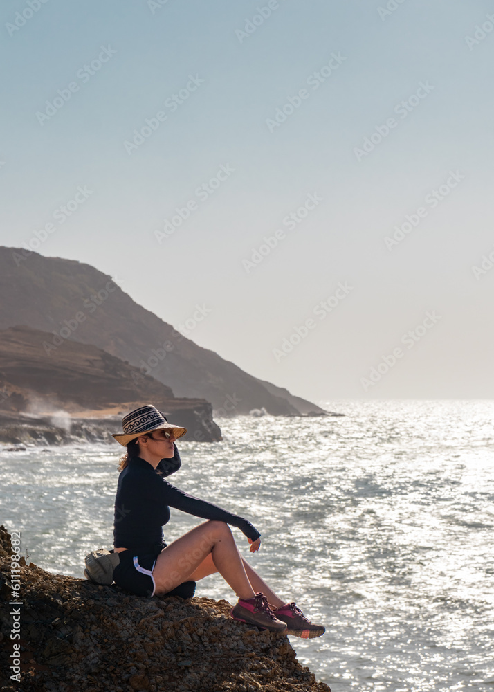 Latina Woman Sitting on Cliff's Edge, Overlooking the Majestic Sea and Desert Mountains of La Guajira, Colombia