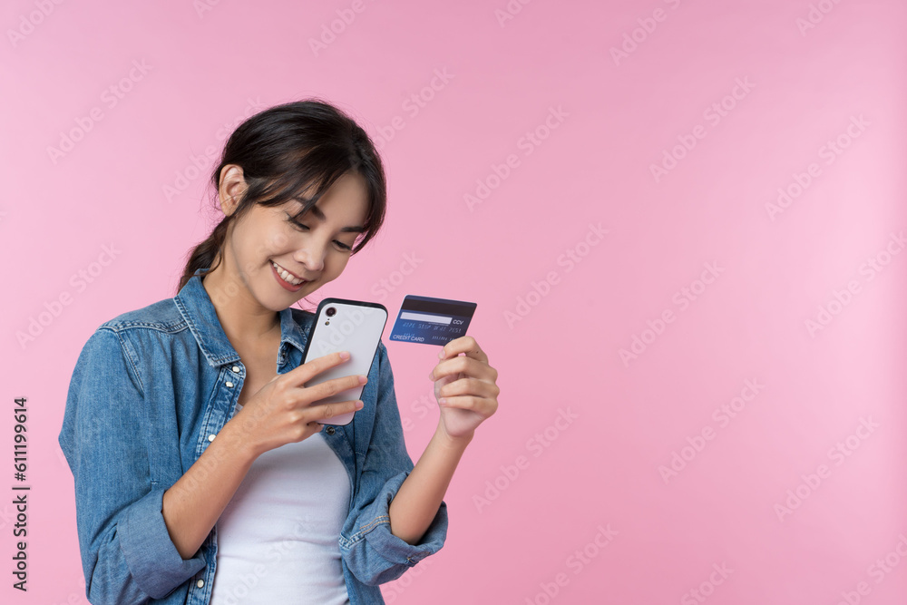 Young beauty Asian woman shopping payment online with credit card on smartphone and she wearing jean and looking at phone isolated on pink background Young beauty Asian woman shopping payment online with credit card on smartphone and she wearing jean and looking at phone isolated on pink background