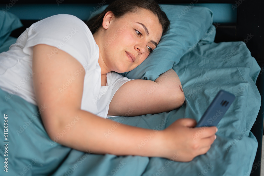 Portrait of young woman with smartphone texting message in bed at home. Technology, communication and people Portrait of young woman with smartphone texting message in bed at home. Technology, communication and people