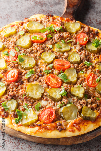 Hot pizza with ground beef, tomatoes, pickled cucumbers and cheese close-up on a wooden board on the table. Vertical
