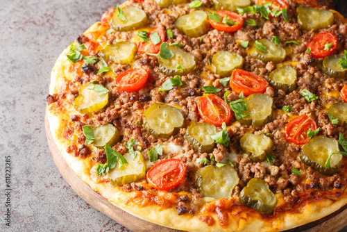 Hamburger pizza with ground beef, tomatoes, pickled cucumbers and cheese close-up on a wooden board on the table. Horizontal