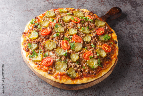 Tasty Pizza is topped with a creamy burger sauce, ground beef, cheese and pickles closeup on the wooden board on the table. Horizontal