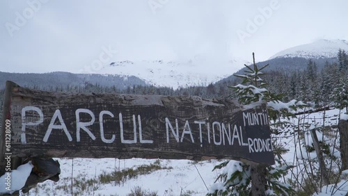 Rustic wooden sign at entrance of Mount Rodnei National Park in Northern Romania, a popular mountain climbing destination. Snow covered rugged terrain in winter. Boom up. photo
