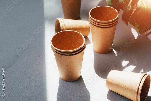 Disposable tableware for eating from environmentally friendly materials. Paper cups on a white table with green leaves in the background. The concept of degradable waste. Top view photo