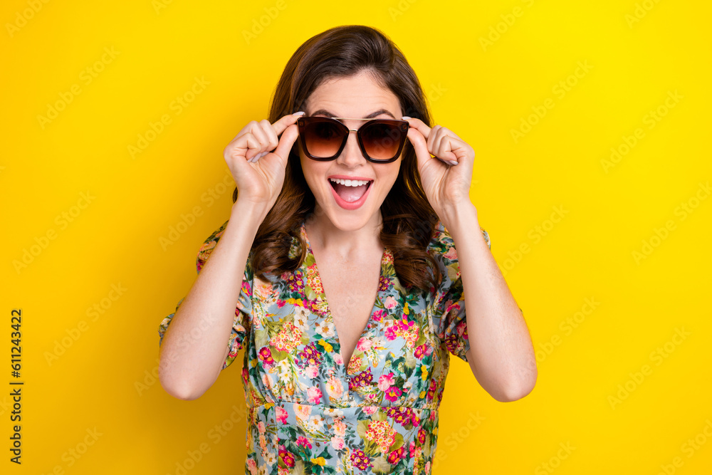 Photo of astonished positive girl open mouth hands touch sunglass isolated on yellow color background Photo of astonished positive girl open mouth hands touch sunglass isolated on yellow color background