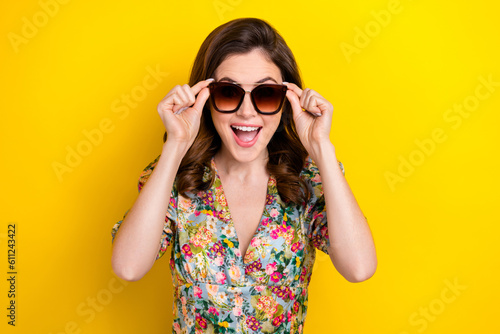 Photo of astonished positive girl open mouth hands touch sunglass isolated on yellow color background