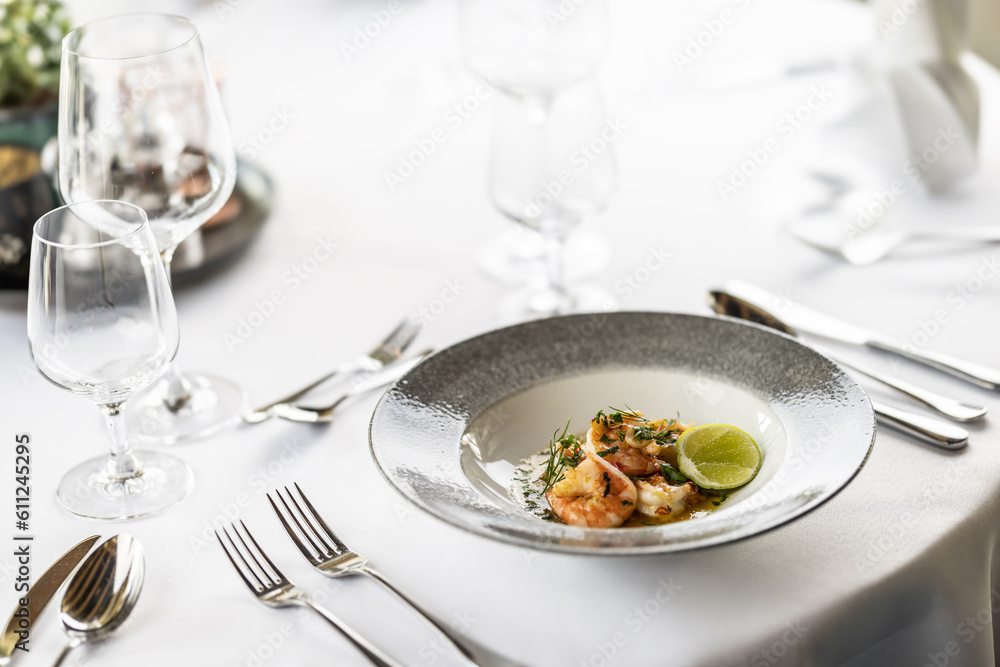 White setting of a formal table in a restaurant with a plate of appetizer in the form of grilled chilli and garlic shrimps
