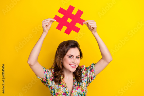 Portrait of cheerful nice person toothy smile arms hold paper hashtag symbol isolated on yellow color background