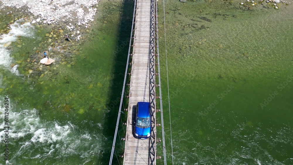 car passes over a wooden Tibetan bridge that joins the river banks - view from the drone in Alagna Val Sesia Piedmont mountains - travel concept journey in adventure natural trip 