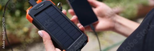 Hands holding solar power bank and mobile phone for recharging closeup. Charge smart phone from solar battery concept