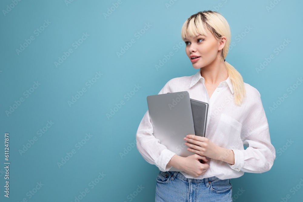 young blond caucasian woman with a short haircut dressed in a white shirt and jeans holds work notebooks and a laptop against the background of copy space. business concept young blond caucasian woman with a short haircut dressed in a white shirt and jeans holds work notebooks and a laptop against the background of copy space. business concept