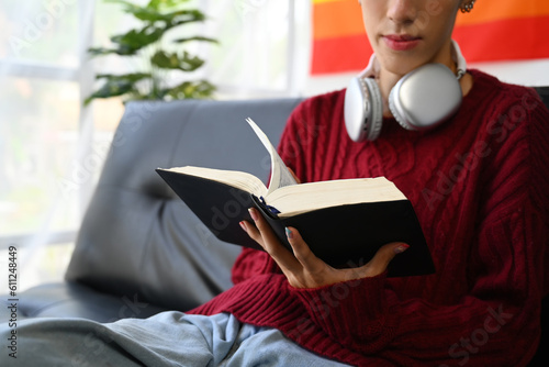 Relaxed young gay man relaxing on couch at home and reading book. LGBTQ, people lifestyle, leisure concept