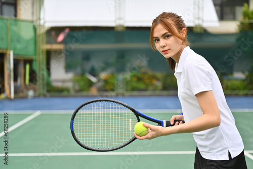 Determined young female tennis player with racket serving ball during match. Outdoor sports and healthy lifestyle concept