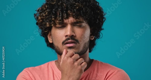 Serious pensive thinkful indian man standing isolated over blue studio background photo