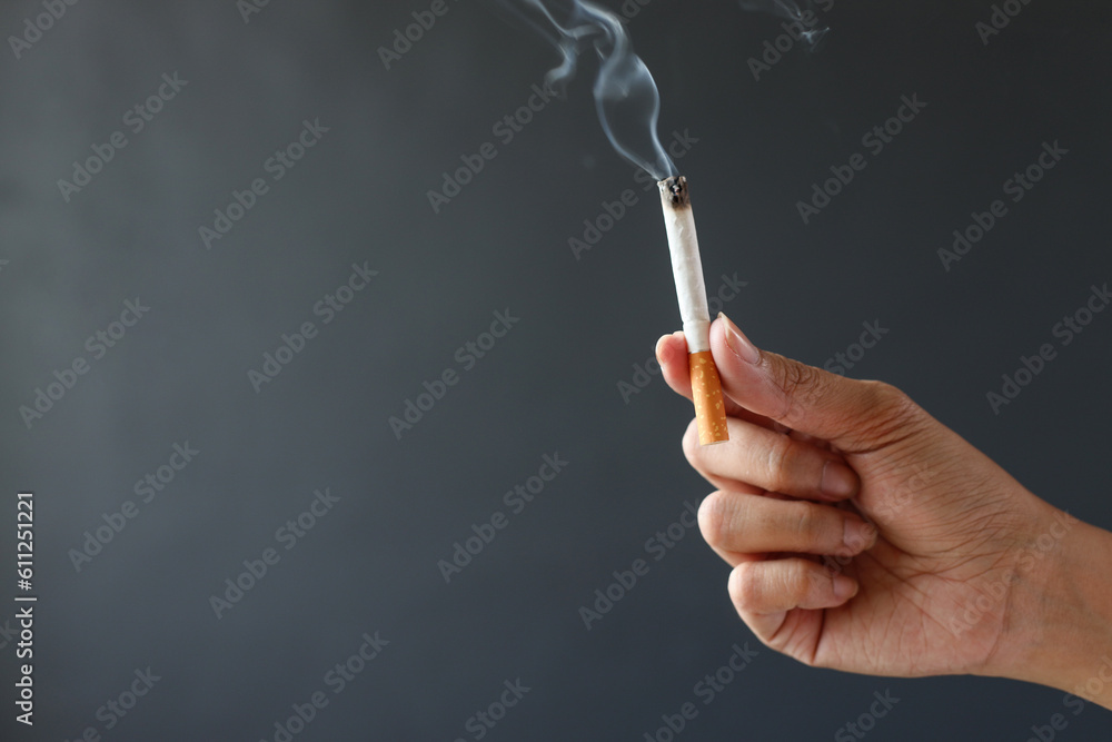 Hand holding smoking cigarette on gray background Hand holding smoking cigarette on gray background