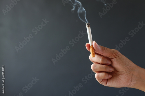 Hand holding smoking cigarette on gray background