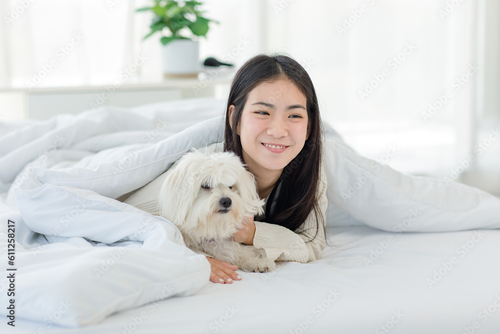 Asian young happy cheerful female owner laying lying down smiling hugging cuddling embracing best friend companion dog white long hair mutt shih tzu under blanket on bed together in bedroom at home Asian young happy cheerful female owner laying lying down smiling hugging cuddling embracing best friend companion dog white long hair mutt shih tzu under blanket on bed together in bedroom at home