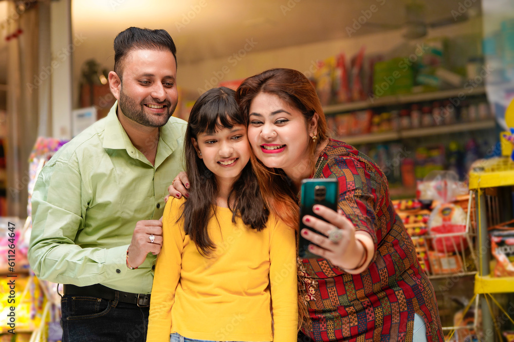 Obraz premium Indian family taking selfie in smartphone at grocery shop.