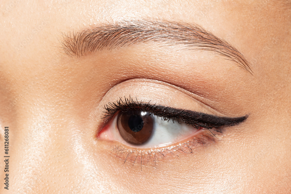 Close up of brown eye of young woman looking aside. Closeup of mixed race ethnicity female eye with eyeliner and healthy smooth under eyes skin. Make-up and antiaging skincare cosmetics advertising. Close up of brown eye of young woman looking aside. Closeup of mixed race ethnicity female eye with eyeliner and healthy smooth under eyes skin. Make-up and antiaging skincare cosmetics advertising.